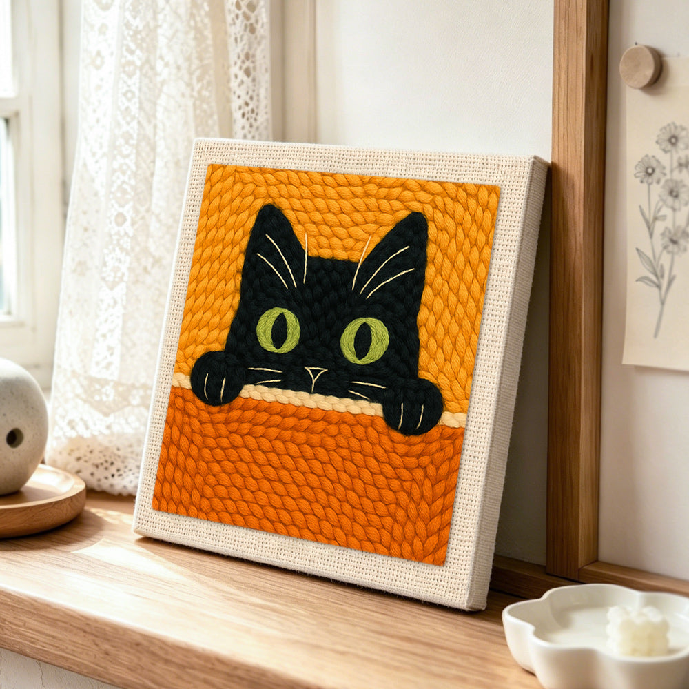 Curious black cat peeking over punch needle artwork displayed on a table