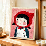 Cute girl in red headscarf punch needle artwork displayed on a table