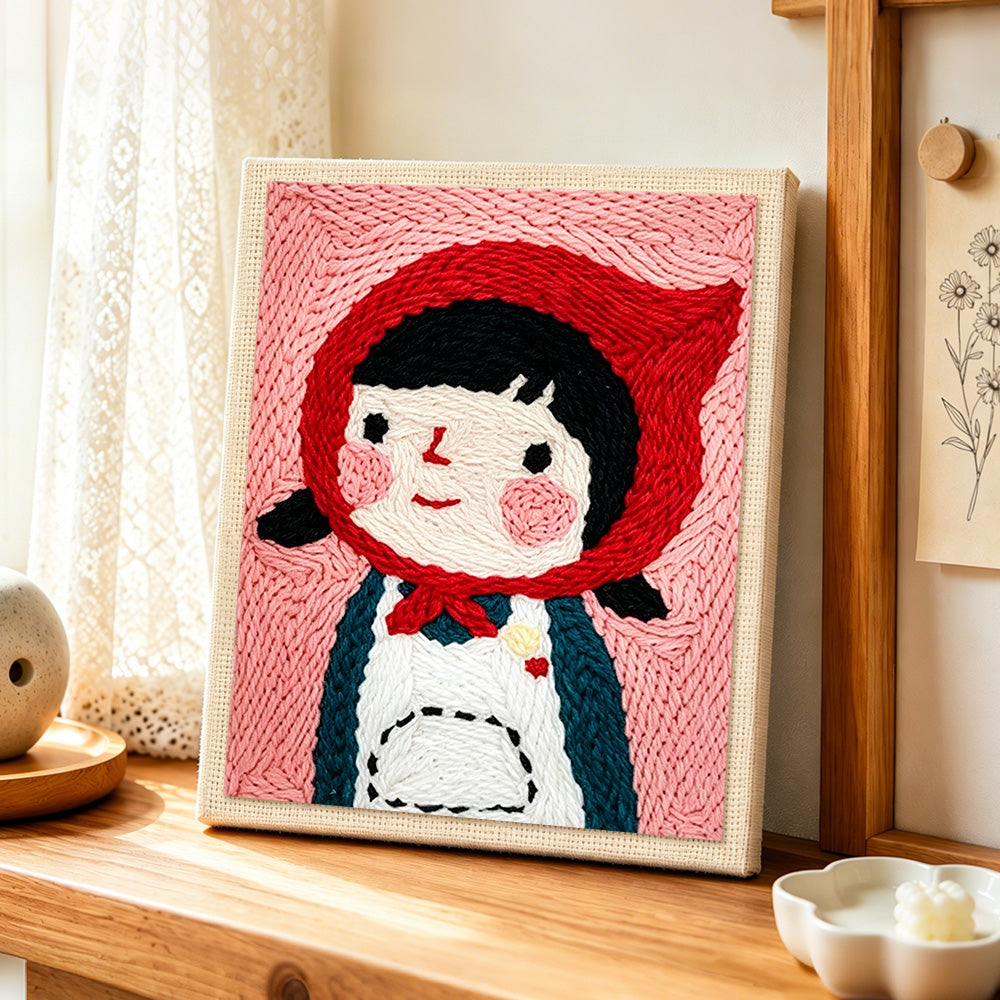 Cute girl in red headscarf punch needle artwork displayed on a table