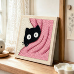 Cute peeking kitten in pink blanket punch needle artwork displayed on a table