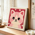 Cute pink and white kitten face punch needle artwork displayed on a table