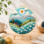 Finished daisy sun and red cottage in the alps needle felting displayed on a wooden easel
