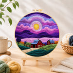 Finished dreamy swirling purple sky and red barn needle felting displayed on a wooden easel