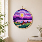Dreamy swirling purple sky and red barn needle felt wall art displayed in a bright home interior