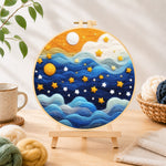 Finished drifting blue clouds and yellow stars needle felting displayed on a wooden easel