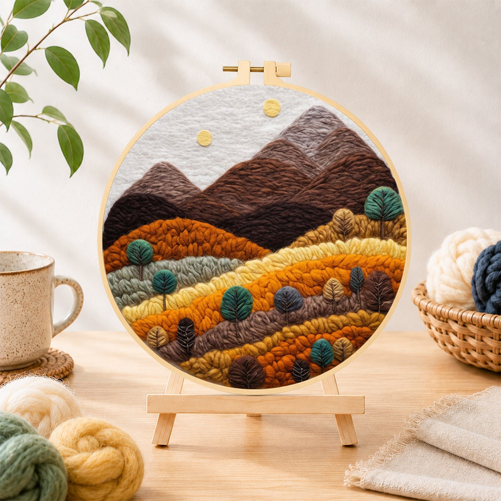 Finished earthy brown and burnt orange mountains with trees needle felting displayed on a wooden easel