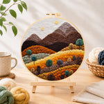 Finished earthy brown and burnt orange mountains with trees needle felting displayed on a wooden easel