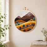 Earthy brown and burnt orange mountains with trees needle felt wall art displayed in a bright home interior