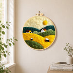 Farmhouses and rolling hills needle felt wall art displayed in a bright home interior