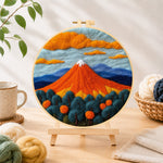Finished fiery red volcano and deep blue trees needle felting displayed on a wooden easel