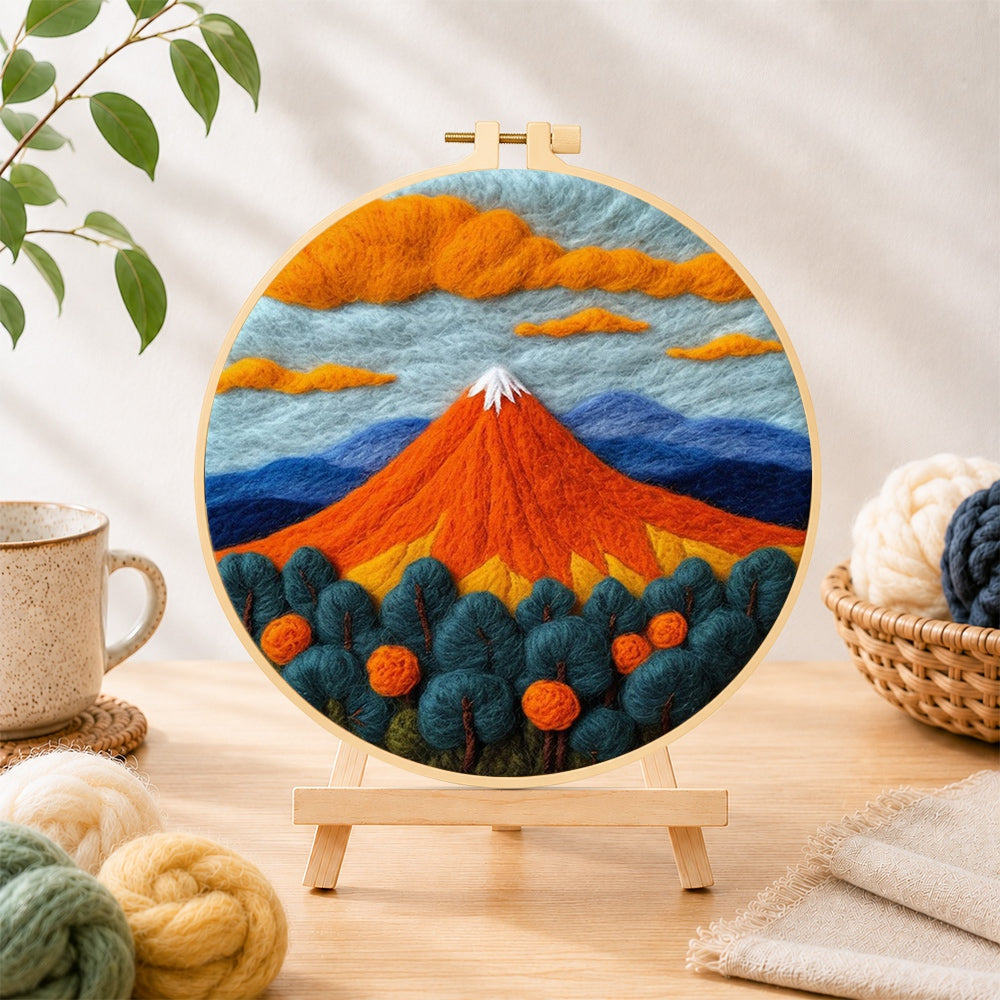 Finished fiery red volcano and deep blue trees needle felting displayed on a wooden easel