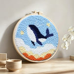 Flying whale in sky with stars and clouds punch needle artwork displayed on a table
