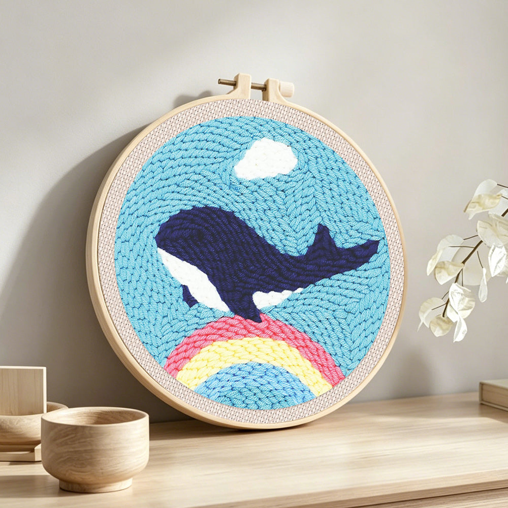 Flying whale over rainbow in blue sky punch needle artwork displayed on a table
