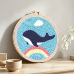 Flying whale over rainbow in blue sky punch needle artwork displayed on a table