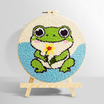 Frog holding a flower punch needle kit for beginners