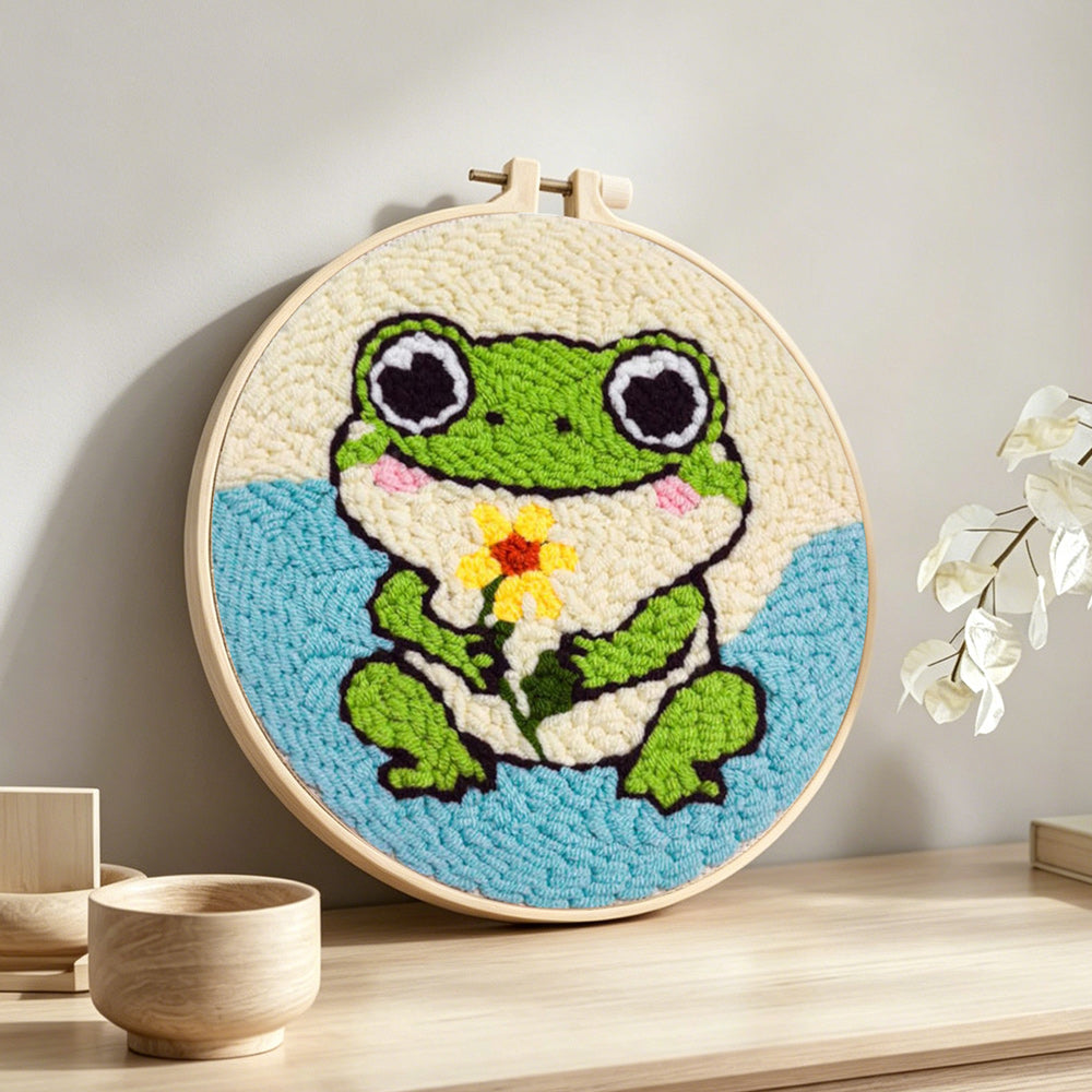 Frog holding a flower punch needle artwork displayed on a table