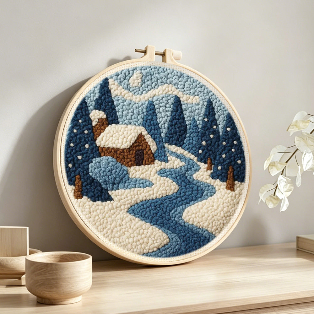 Frozen blue forest and cosy cabin punch needle artwork displayed on a table