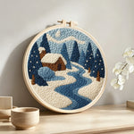 Frozen blue forest and cosy cabin punch needle artwork displayed on a table