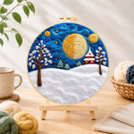 Finished giant spiral half-moon and snowy tower house needle felting displayed on a wooden easel