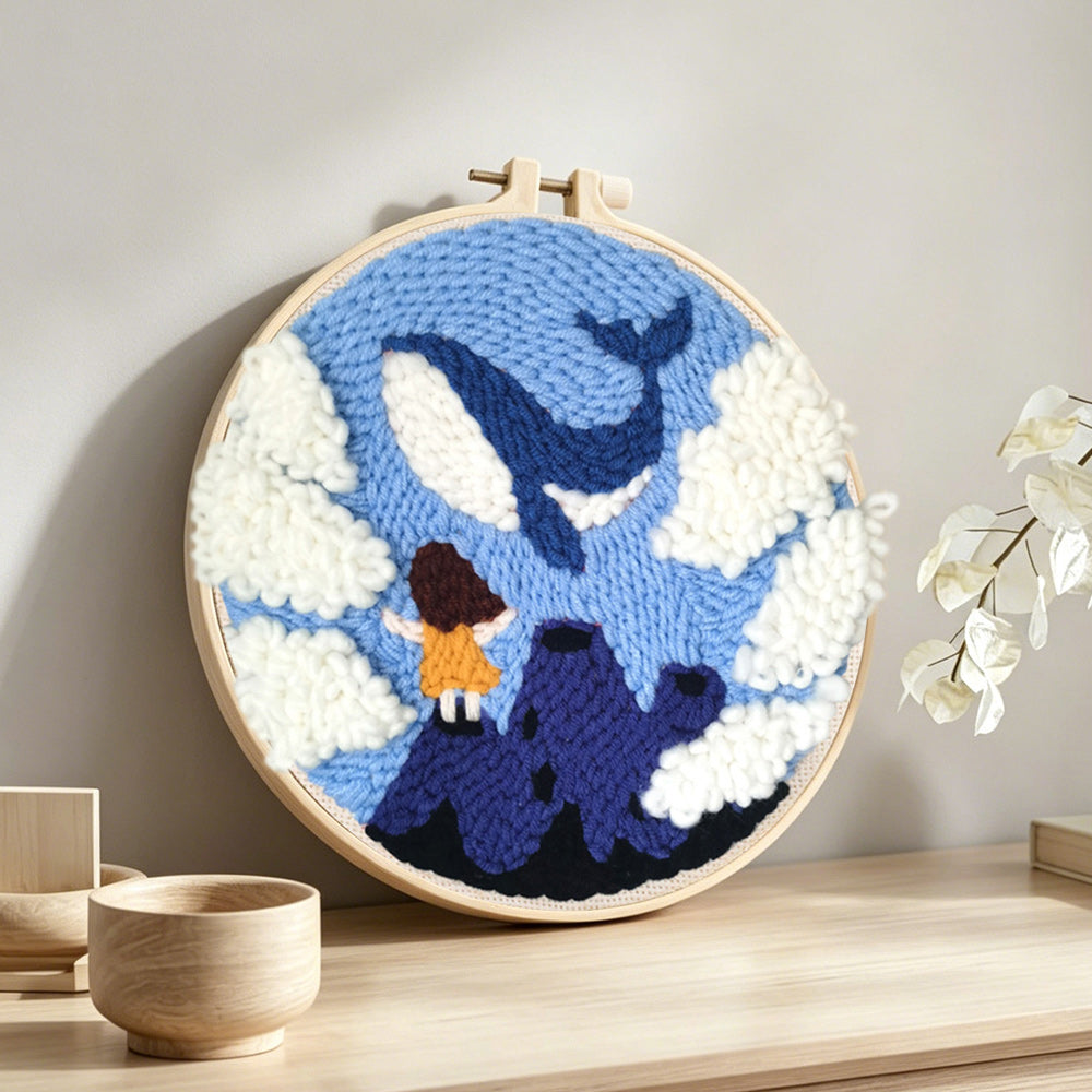 Girl standing on mountain peak watching whale in sky punch needle artwork displayed on a table