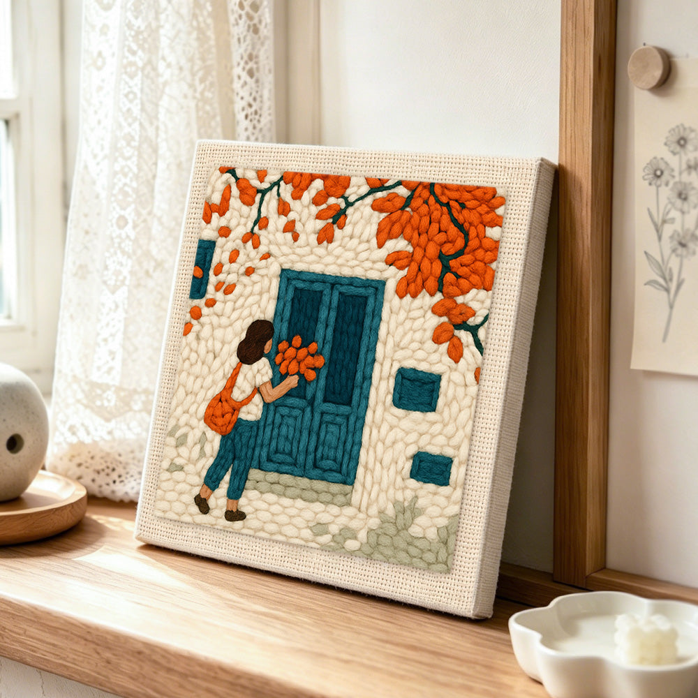 Girl with orange leaves at blue door punch needle artwork displayed on a table