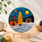 Finished golden christmas tree and snowy cabins needle felting displayed on a wooden easel
