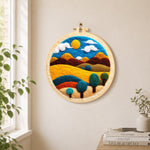Golden sun and swirling tree hills needle felt wall art displayed in a bright home interior