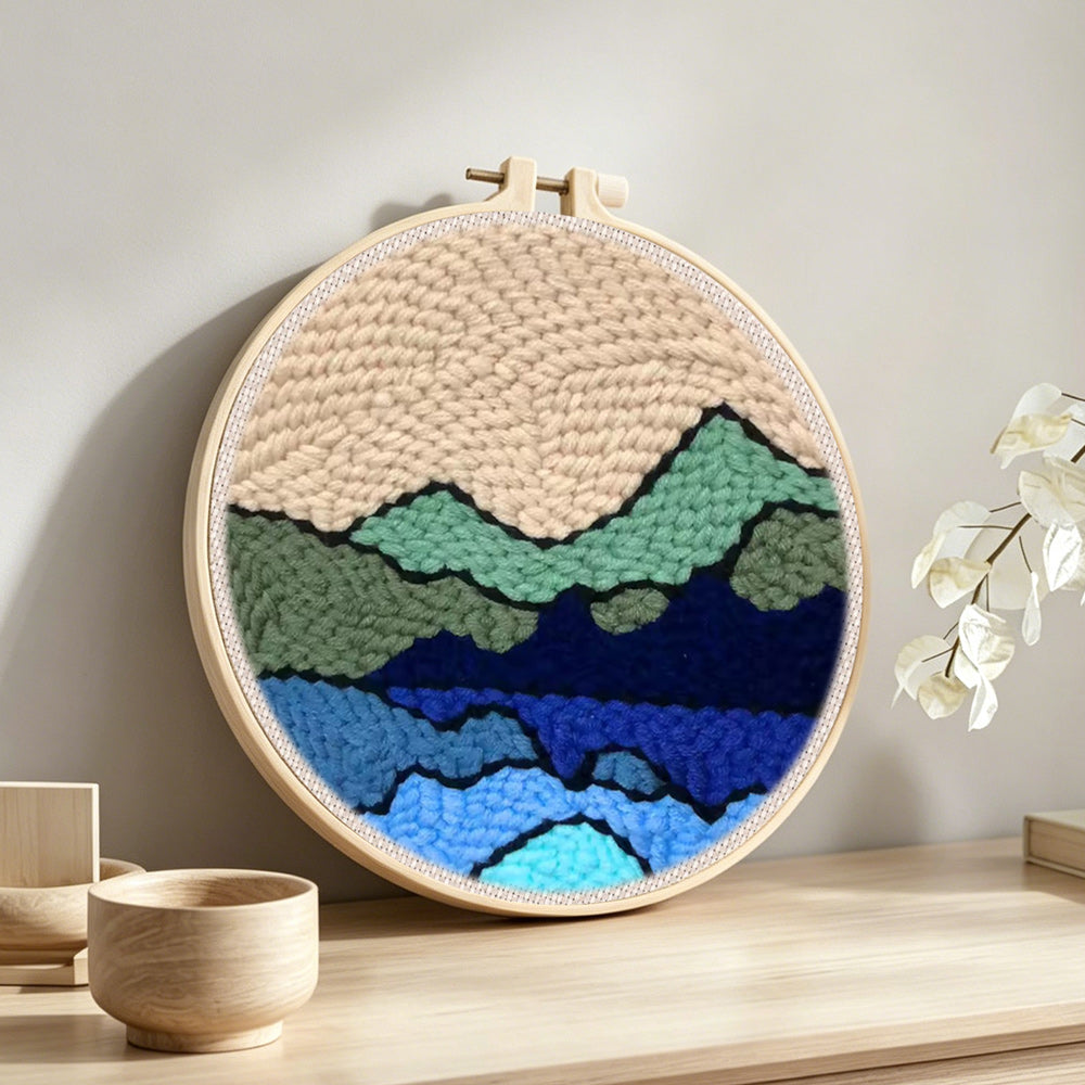 Green and blue mountain range punch needle artwork displayed on a table