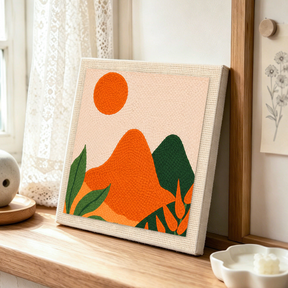 Green and orange hills with leaves punch needle artwork displayed on a table