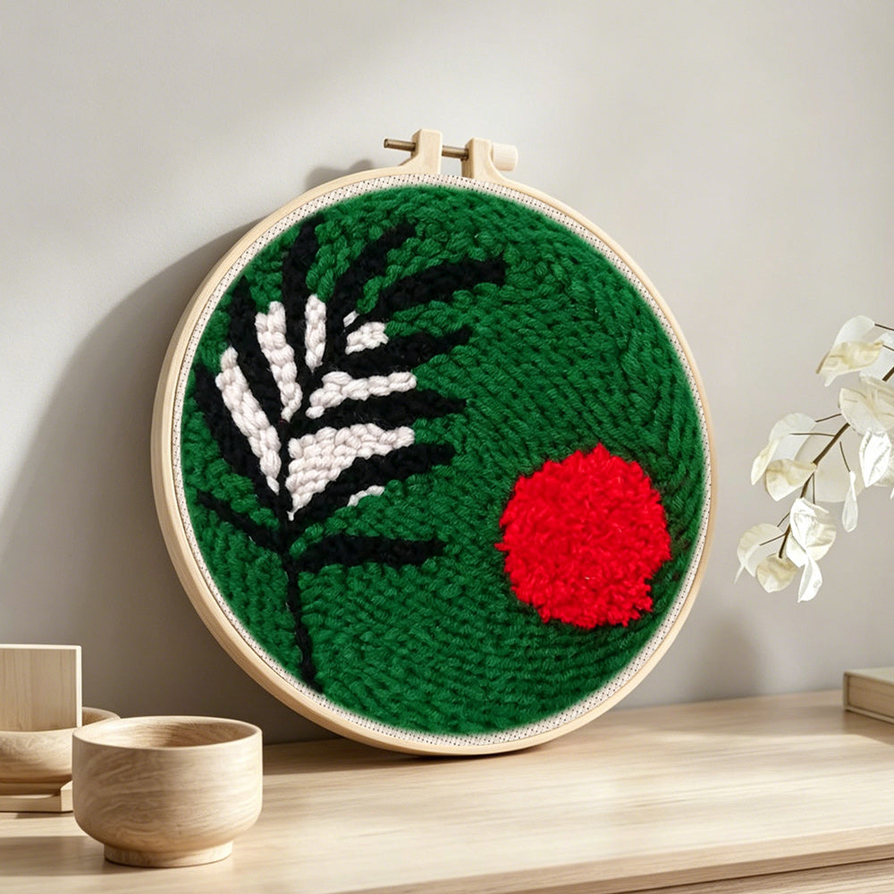 Green botanical with red sun punch needle artwork displayed on a table