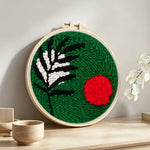 Green botanical with red sun punch needle artwork displayed on a table