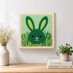 Finished green bunny hiding in grass artwork displayed on a wall