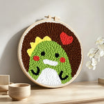 Green dinosaur and red heart punch needle artwork displayed on a table