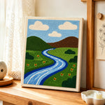 Green grassland and peaceful river punch needle artwork displayed on a table