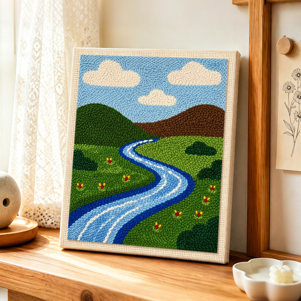 Green grassland and peaceful river punch needle artwork displayed on a table