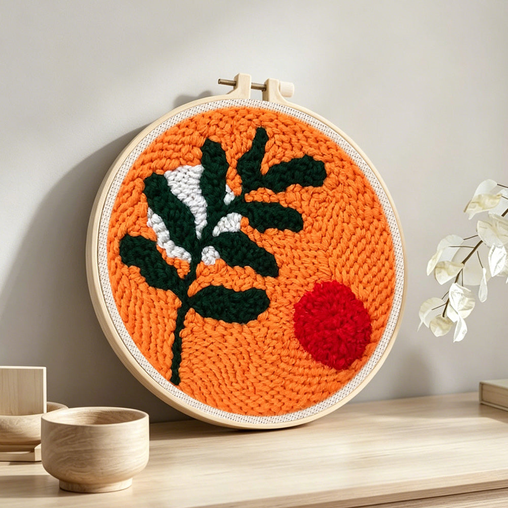 Green leaves and red sunr punch needle artwork displayed on a table