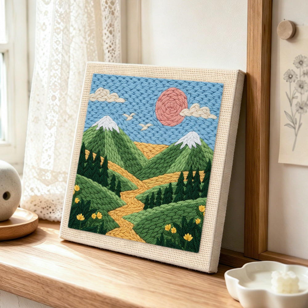 Green mountains and yellow wildflowers punch needle artwork displayed on a table