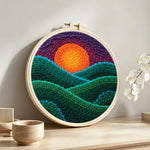 Green rolling hills at sunset punch needle artwork displayed on a table