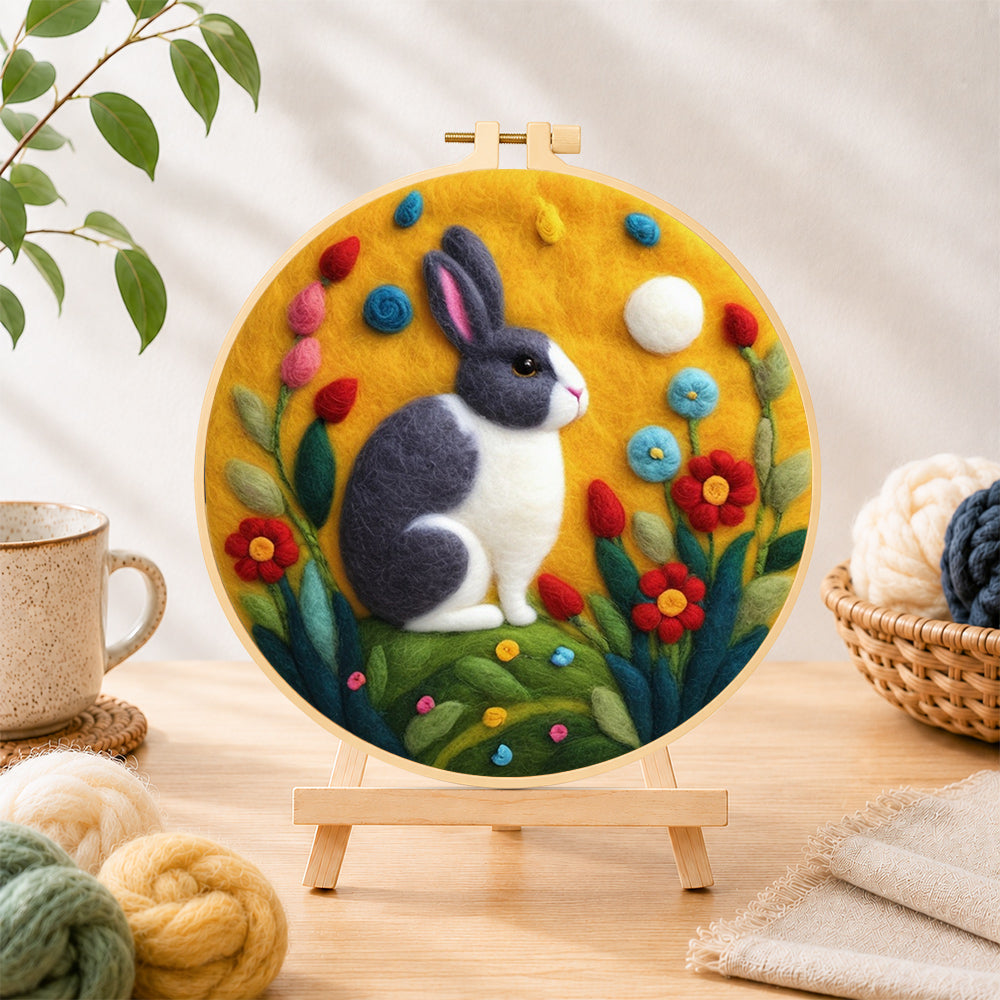 Finished grey and white rabbit among flowers needle felting displayed on a wooden easel