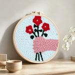 Hand holding red flowers punch needle artwork displayed on a table