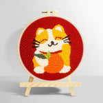Happy cat holding an orange punch needle kit for beginners