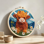 Highland cow, mountains and daisies punch needle artwork displayed on a table