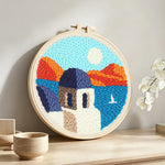 House by the sea and mountains punch needle artwork displayed on a table