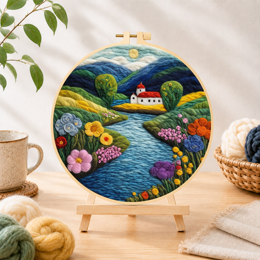 Finished idyllic mountain village and river needle felting displayed on a wooden easel