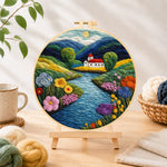 Finished idyllic mountain village and river needle felting displayed on a wooden easel