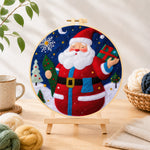 Finished jolly santa holding gift and tree needle felting displayed on a wooden easel