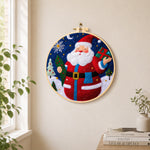 Jolly santa holding gift and tree needle felt wall art displayed in a bright home interior