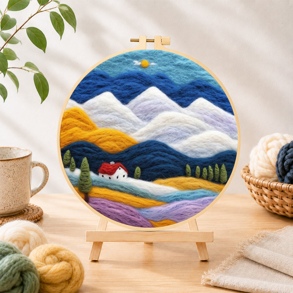 Finished layered mountains and red-roof cottage needle felting displayed on a wooden easel