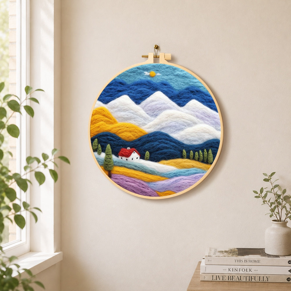 Layered mountains and red-roof cottage needle felt wall art displayed in a bright home interior