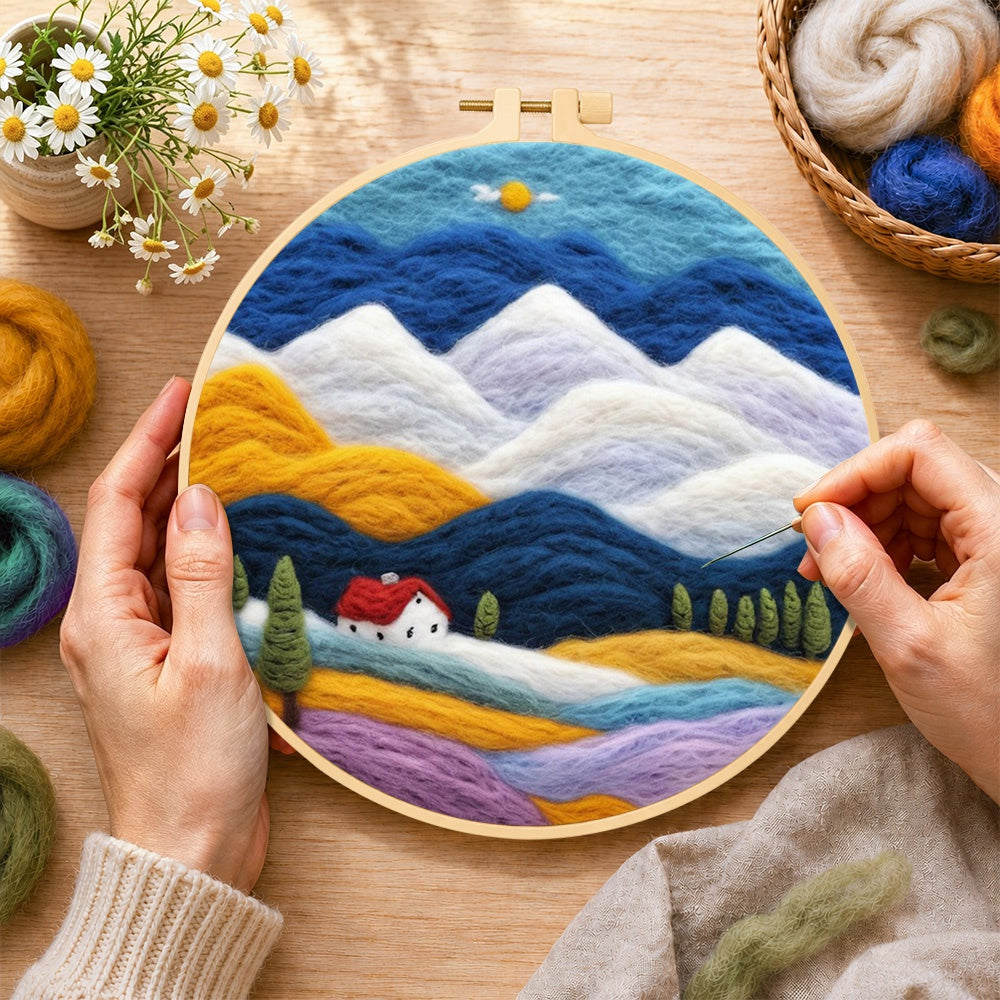 Creating the layered mountains and red-roof cottage wool painting by hand with a felting needle